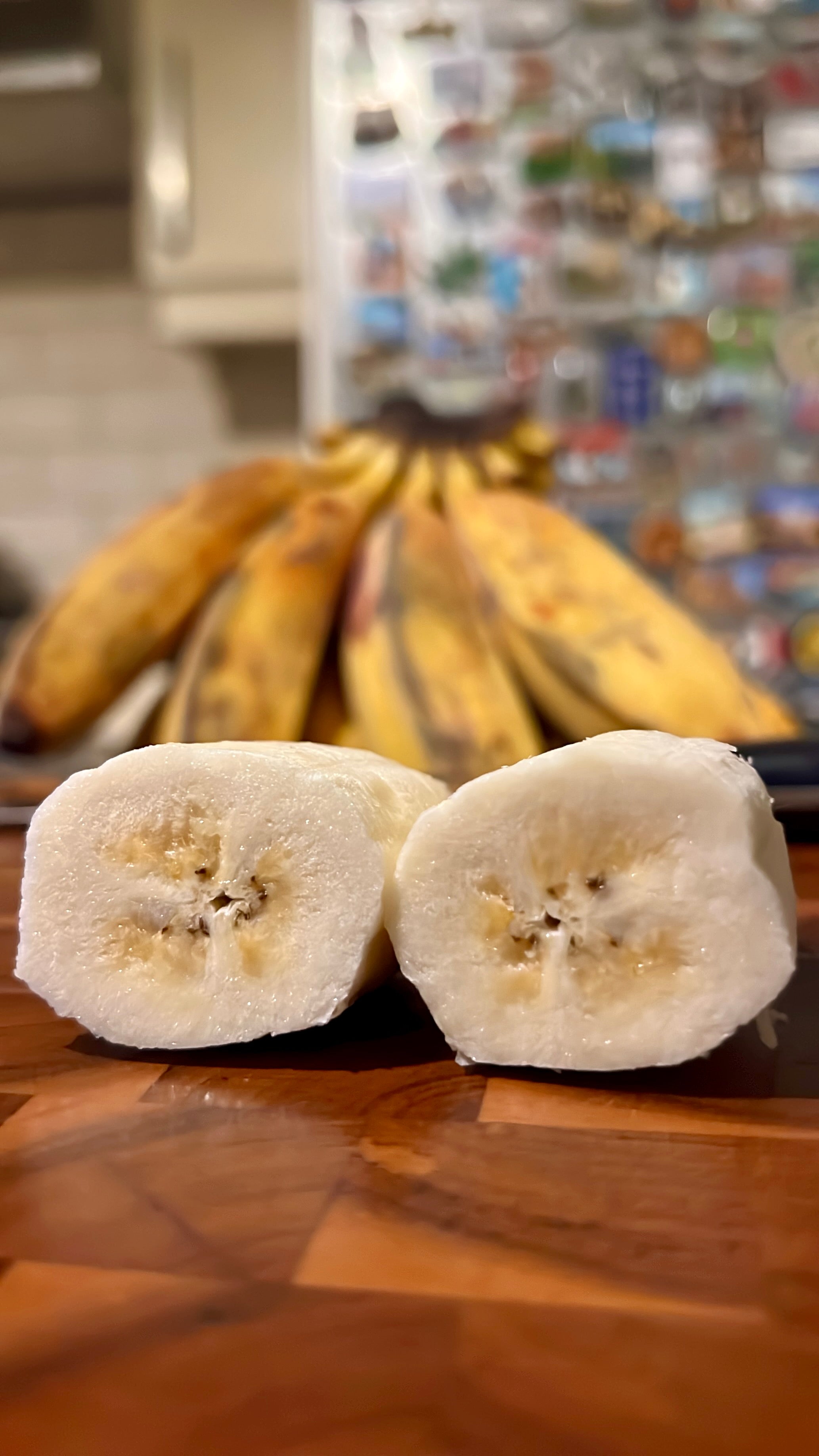 Ripe Saba banana cut in half showing firm white flesh, with a ripe bunch in the background, from Island Mango Ireland.